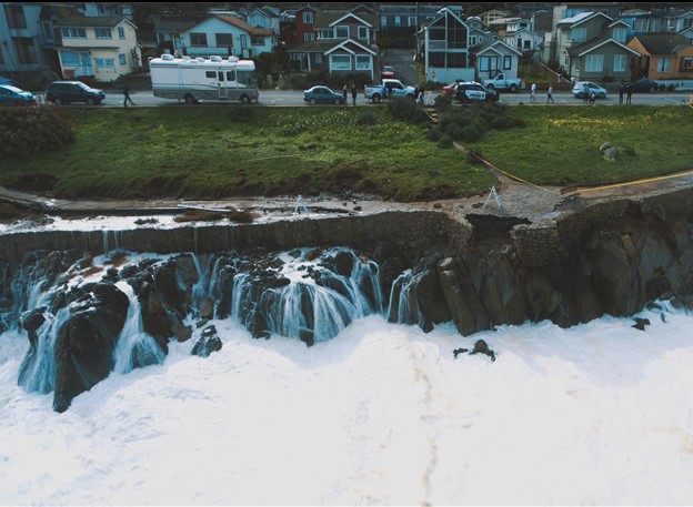 An image of wave action in Pacific Grove battering the shoreline near a neighborhood.