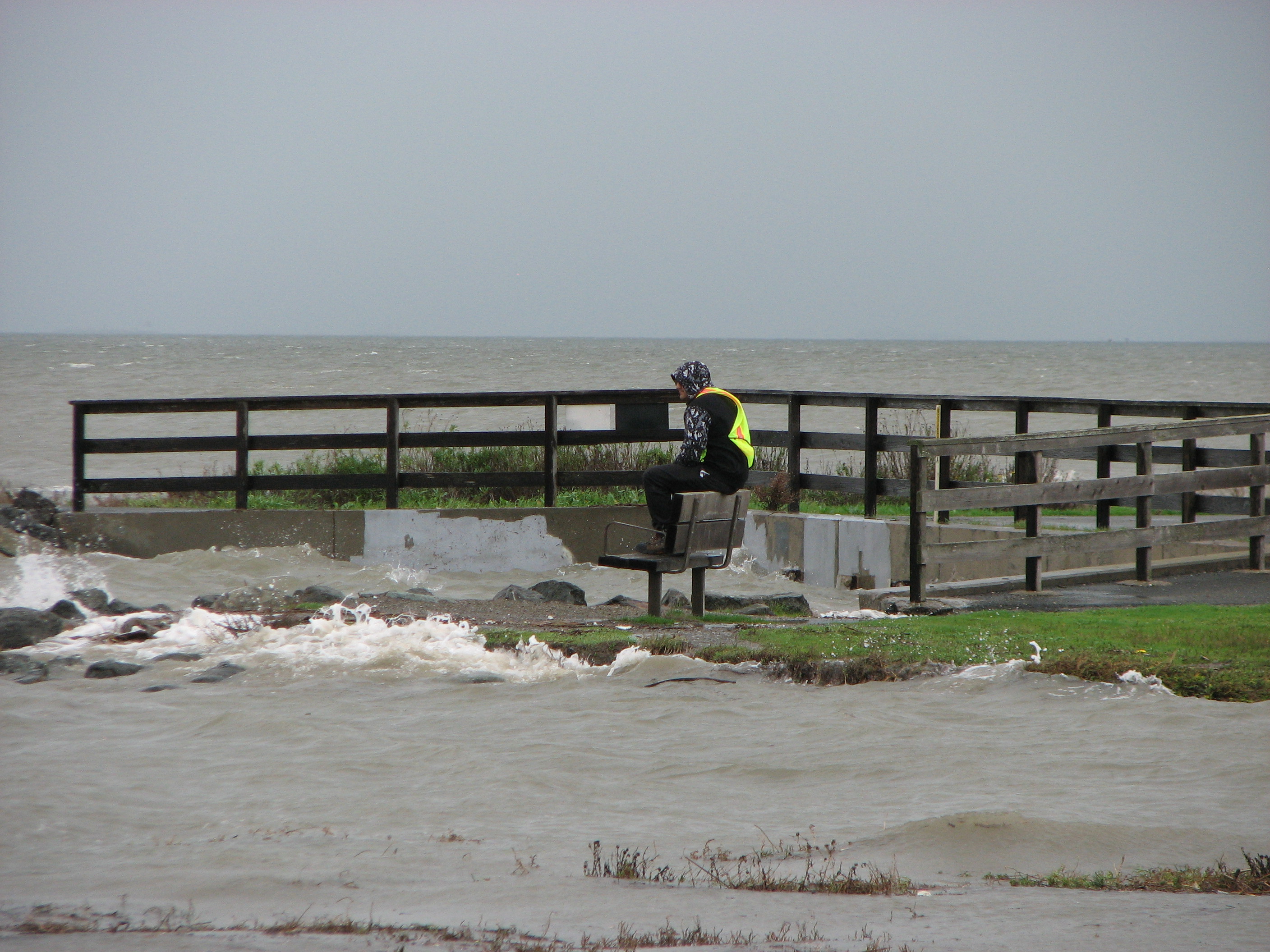 A worker sitting on a shoreline bench, surrounded by waves.