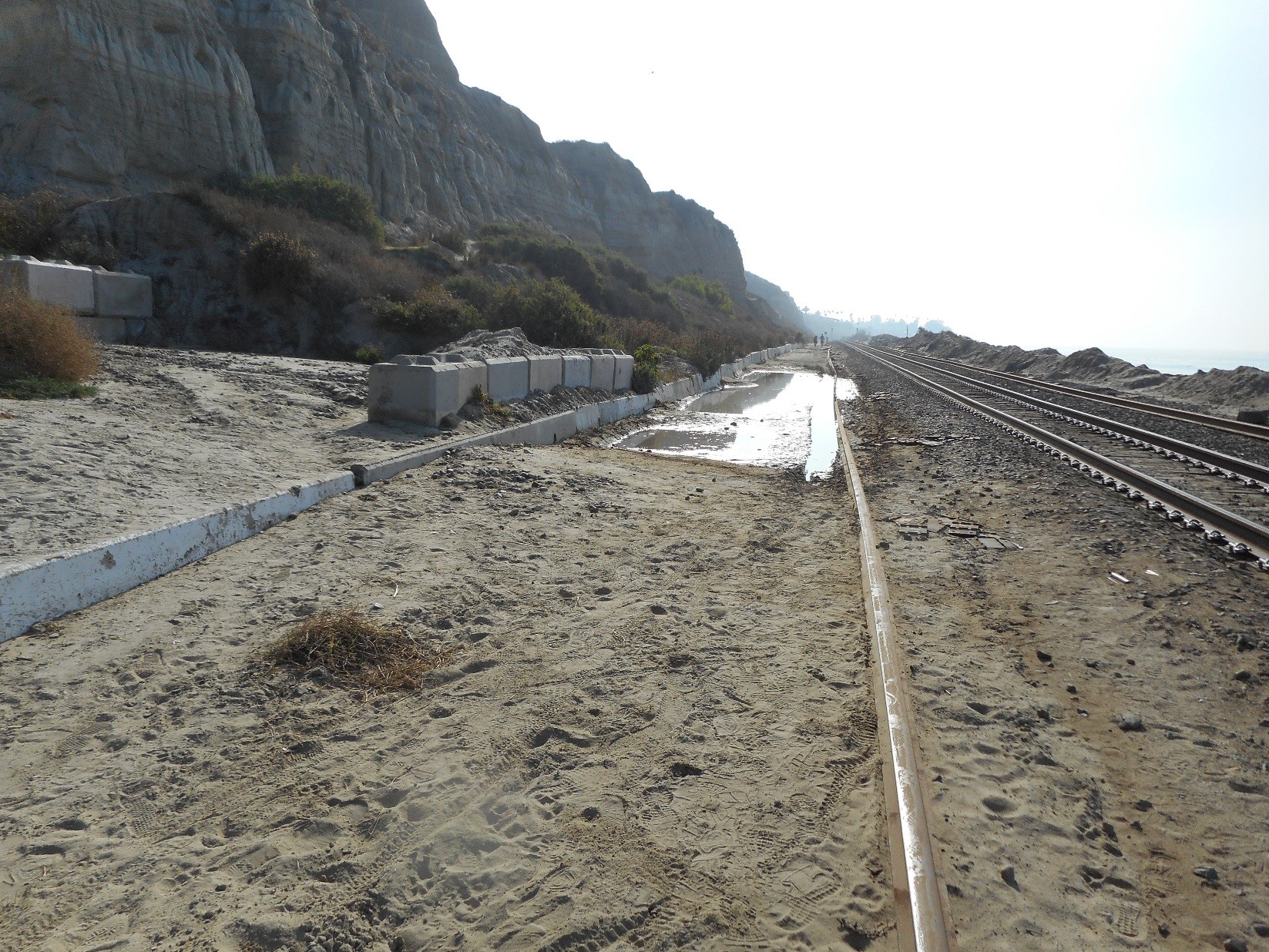 Flooding and erosion along an embankment above a rail line.